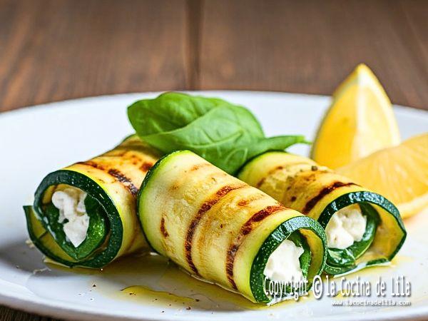 Fotografía de un plato de rollitos de calabacín rellenos de queso y hierbas, presentados en un plato blanco. Las láminas de calabacín están ligeramente doradas y crujientes