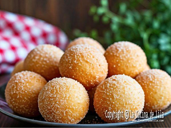 Buñuelos caseros dorados cubiertos de azúcar, mostrando una textura crujiente.